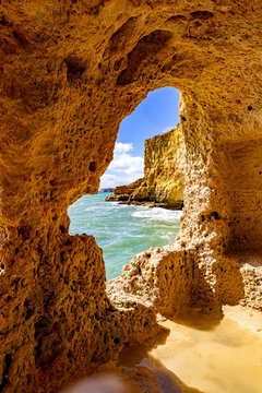 View of cavernous rock formations frame the sparkling turquoise ocean waters and rugged coastline, Algarve, Gruta da Boneca, Faro, Portugal.
