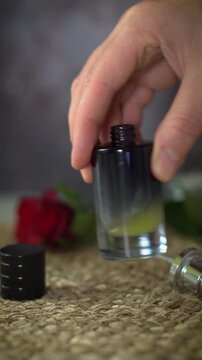 Close-up vertical video of mixing essential oil blend in black perfume bottle. Natural homemade fragrance creation with luxury aesthetic and red rose on dark and beige background.