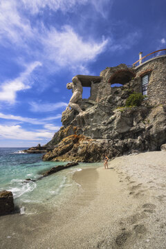View of a sculpted titan emerges from rugged cliffs overlooking the serene beach where turquoise waters meet the sandy shore, Monterosso al Mare, Liguria, Italy.