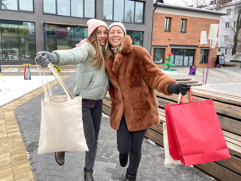 Two cheerful friends holding shopping bags outdoors in winter. Joyful mood, lifestyle, and shared happiness during city leisure and holiday activities.