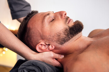 Fototapeta premium Male client receiving a relaxing massage therapy session, with a therapist's hand gently supporting his neck, creating a serene and calming atmosphere for wellness and relaxation