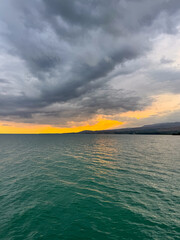 Fototapeta premium Sunset at Issyk Kul Lake in Kyrgyzstan. Bright sun breaking through clouds reflecting in clear turquoise water.