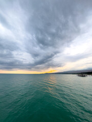 Fototapeta premium Sunset at Issyk Kul Lake in Kyrgyzstan. Bright sun breaking through clouds reflecting in clear turquoise water.