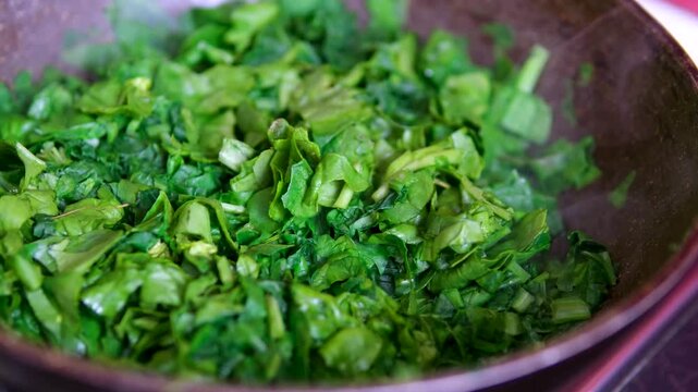 The process of washing and stewing spinach: wash men's hands under water, cut into pieces, throw in a frying pan, stir, prepare for freezing, make spinach pie