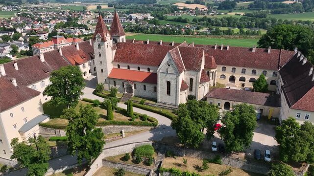 Aerial summer scenery of Sankt Paul im Lavanttal with monastery complex, rooftops, valley landscape, green hills, calm cinematic drone movement, warm atmospheric tones