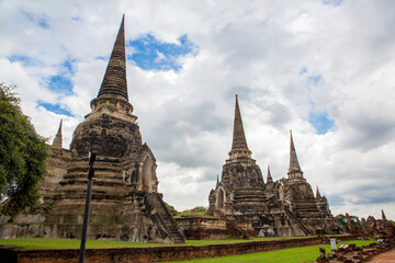 Fototapeta premium The three iconic restored chedis (stupas) at Wat Phra Si Sanphet in Ayutthaya, Thailand. The massive, bell-shaped structures stand in a row on a raised platform covered in green grass. Cloudy day.