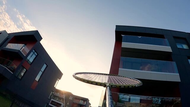 Badminton player strikes shuttlecock in slow motion near modern buildings