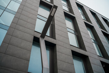 Obraz premium Modern office building facade with geometric windows and minimalist street lamp. Contemporary urban architecture with clean lines, dark panels and glass reflecting soft daylight.