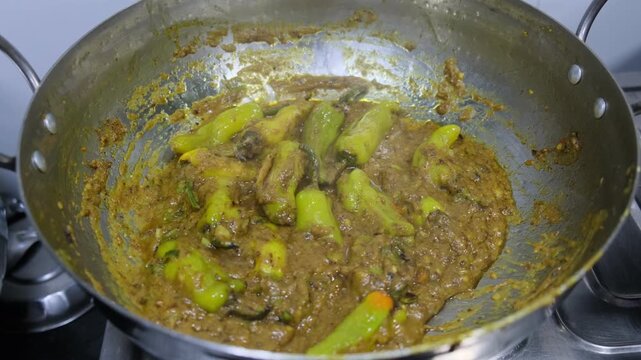 Traditional Indian stuffed green chili curry (Bharwan Mirch) cooking in a stainless steel wok