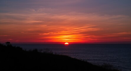 Sunset silhouette over calm ocean horizon with vibrant sky colors