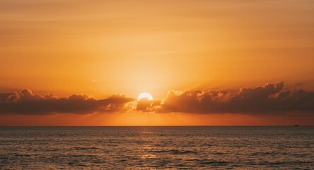 Obraz premium Sunset casting warm orange hues over calm sea and gentle white clouds