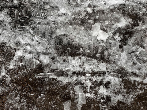 Broken icicles and chunks of ice fallen from a rooftop during thaw, scattered on dark wet pavement. Dangerous winter conditions in urban environment