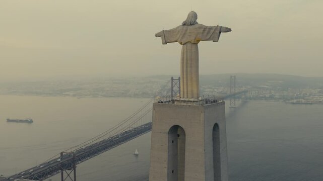 Drone view of the Christ the King monument in Almada, Portugal, with the 25 de Abril Bridge spanning the Tagus River and Lisbon visible in the background.
