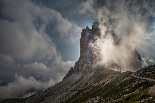 View of jagged peaks pierce through swirling clouds, a rugged landscape with a winding path carving through the mountainside, a scene of dramatic beauty, Tre Cime, Veneto, Italy.