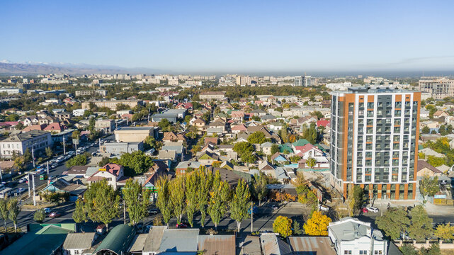 Aerial panorama of Bishkek, Kyrgyzstan with Soviet-era blocks, private houses, and distant smokestacks illustrating Central Asian urban growth and mixed development.
