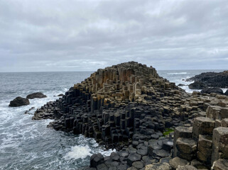 The Giant's Causeway, a natural wonder of hexagonal basalt columns on the coast of Northern Ireland, meeting the turbulent sea under a cloudy sky.