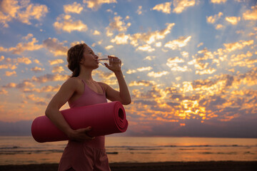 Naklejka premium Athlete woman drinking water at the beach during summer vacation
