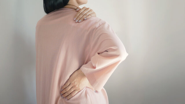 Businesswoman stood there, experiencing simultaneous back and shoulder pain. She displayed a pained expression, using both hands to support and gently massage her neck to relieve the tension