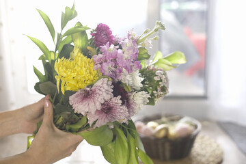 Hands Presenting A Fresh Spring Bouquet near basket with Easter eggs