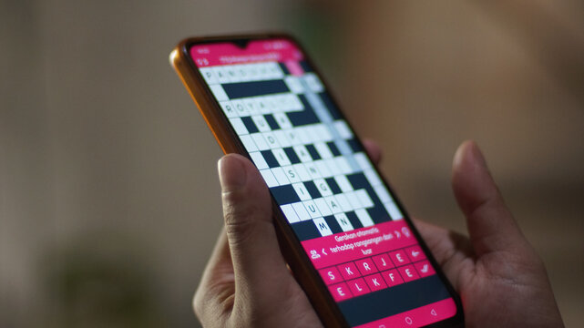 Close-up of a person's hand using his cell phone to do a crossword puzzle, utilizing technology for cognitive stimulation