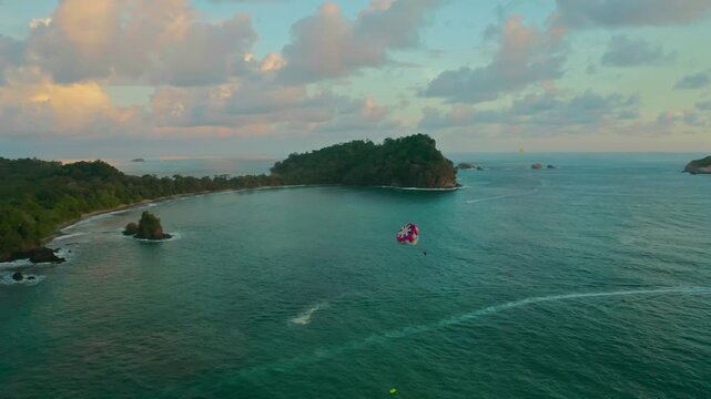 Drone view of parasailing during sunset at Manuel Antonio National Park Costa Rica, surrounded by lush shoreline, stunning beach and turquoise blue ocean