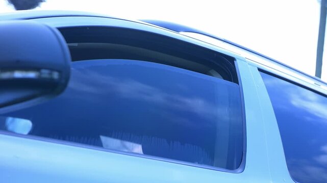 A serene view emerges from a car window, showcasing a bright blue sky dotted with clouds. Sunlight filters in, hinting at upcoming adventures and journeys. Raising up a car door window.