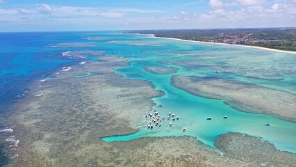 Obraz premium Fantastic aerial view of the turquoise waters of Toque beach with dozen of small boats with tourists on the natural pools formed among coral reefs in Milagres route near Maceio, Alagoas State, Brazil 