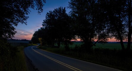 Twilight scene of a meandering country road lined with trees on a warm summer night