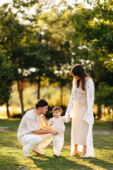 Fototapeta premium Young Family Walking in Park at Golden Hour Helping Toddler Take First Steps