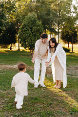 Fototapeta premium Happy Young Family Watching Toddler Run Toward Parents In Sunny Park