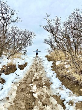 Rear view of a man standing on a snowy and muddy path with his arms outstretched, Ensign Peak Trail, Salt Lake City, Utah, USA