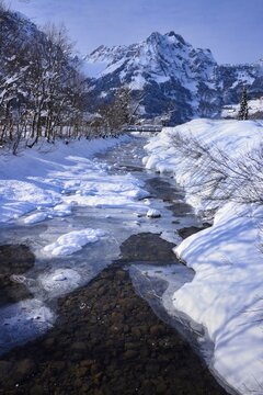 Alpine river flowing through a rural winter landscape with a snowy mountain backdrop, Engelberg, Switzerland