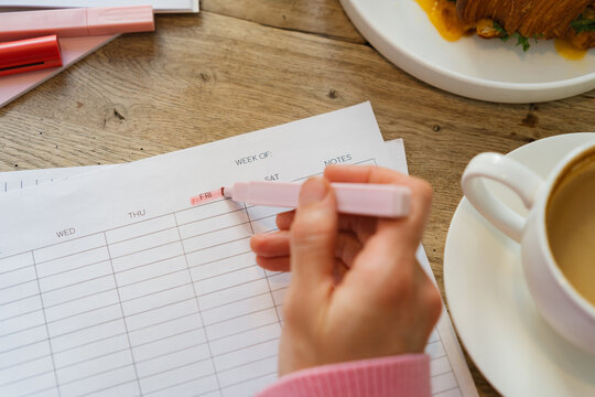 Overhead view of a woman sitting at a table with a cappuccino and a savoury croissant highlighting Friday on a weekly planner