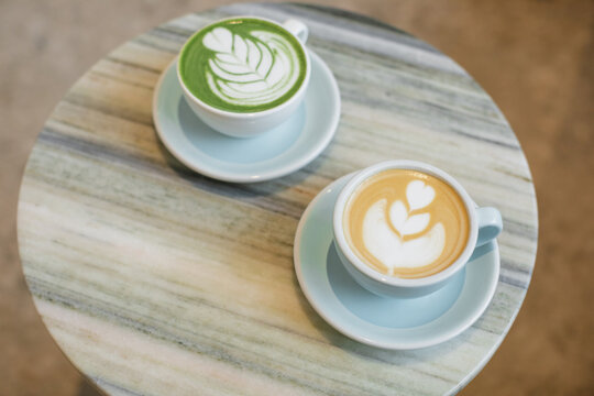 Close-up of a matcha latte and a cappuccino with floral latte art decoration on a table