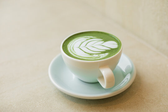 Close-up of a cup of hot matcha latte with floral latte art decoration on a table