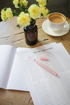 Close-up of a to do list and highlighter pen, a cup of coffee and bunch of flowers in a vase on a wooden table