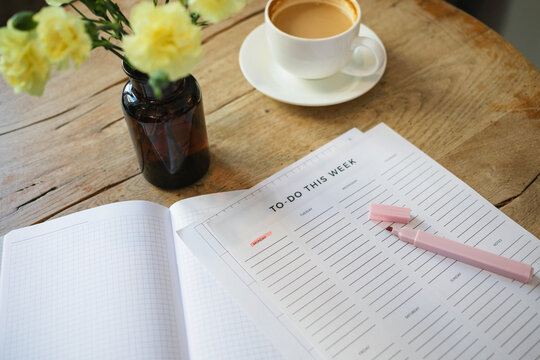 Close-up of a to do list and highlighter pen, a cup of coffee and bunch of flowers in a vase on a wooden table