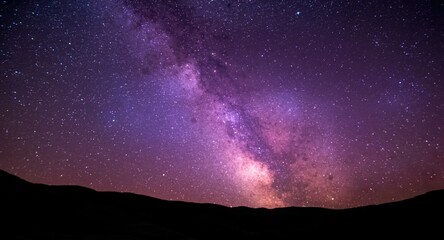 Fototapeta premium Purple Milky Way galaxy stretching across vibrant summer night sky filled with stars and hills