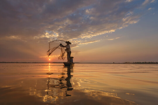 Silhouette of two fisherman in a fishing boat casting a fishing net at sunrise, Thailand