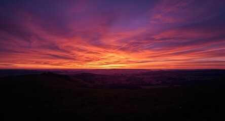 Fototapeta premium Sunset landscape panorama showing vibrant violet and orange sky hues over gently rolling hills