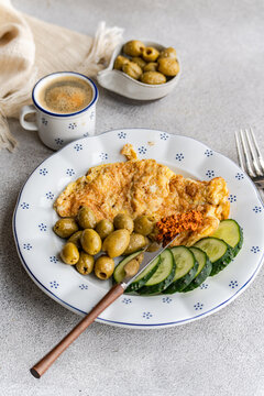 Overhead view of a greek style breakfast with an omelette, cucumber, green olives, red pepper sauce and a cup of black coffee