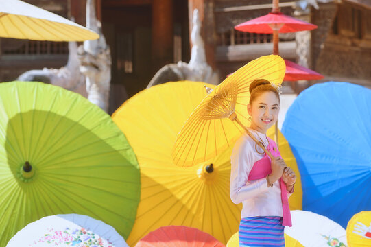 Side view of a smiling woman in traditional Lanna Thai clothing Holding a Handmade paper parasol, Wat Intharawat, Chiang Mai, Thailand