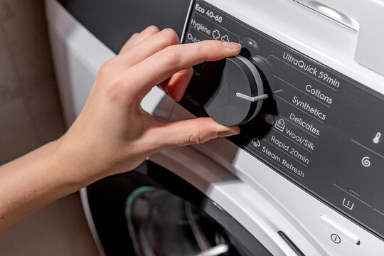 Woman selecting washing machine wash program on control panel. Adult female hand turning front loading appliance dial. Domestic laundry concept for home, cleaning, household lifestyle..