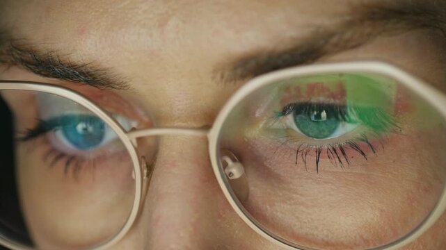 Intense close up woman eyes in glasses looking at screen, with reflections of colorful data charts, graphs on lenses, indicating focus on analytics, digital work. Woman eyes looking at computer screen