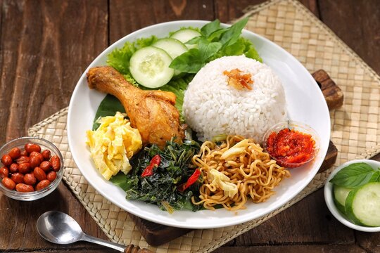  nasi rames featuring steamed white rice served with assorted side dishes including fried chicken, sambal, vegetables, and egg