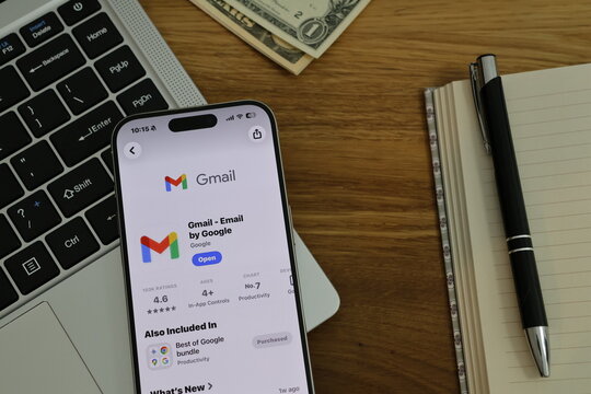 Kiel, Germany - 02-25-2026: A smartphone displaying the Gmail email app for inbox and messaging in App Store displayed on smartphone placed on top of laptop on wooden desk