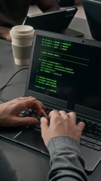 Vertical shot of hands of anonymous male software developer programming on laptop at work table during workday with IT team