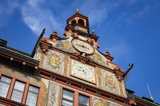 View of the Tubingen Town Hall's ornate facade against a crisp blue sky, showcasing its clocks, coats of arms, and vibrant orange trim, Tubingen, Baden-Wurttemberg, Germany.