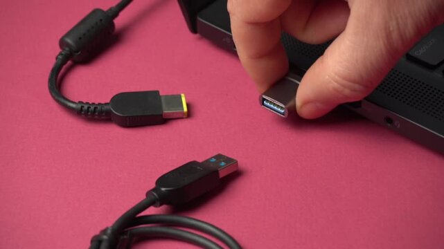 Hand connects USB cable to laptop port, showcasing the process of plugging in various connectors for data transfer and charging