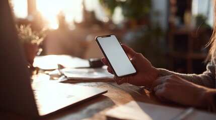 Holding a smartphone while sitting at a desk with papers and a laptop